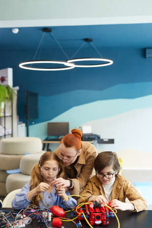 Vertical portrait of female teacher helping children building robot in engineering class at school, copy spaceの写真素材