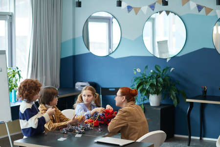 Wide angle view at group of children building robot in engineering class with female teacher, copy...