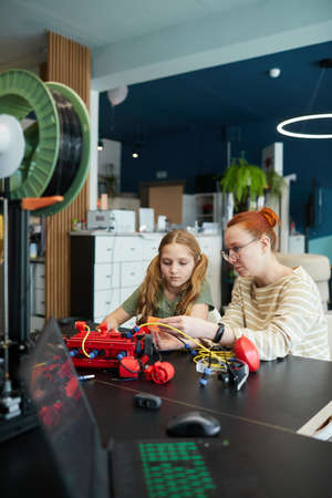 Vertical portrait of young female teacher helping girl building robot during engineering class at modern schoolの写真素材