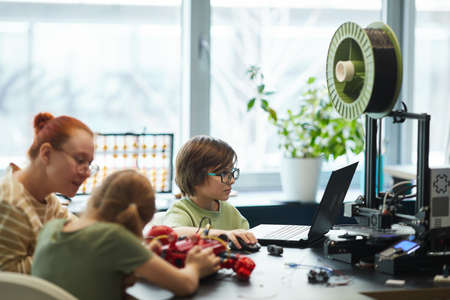 Side view portrait of children 3D printing parts for robots during engineering class at modern school, copy spaceの写真素材