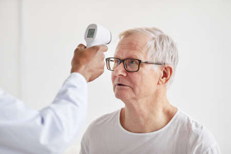 Unrecognizable doctor checking temperature of patient in hospital and pointing infrared thermometer...