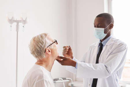 Portrait of young African-American doctor taking COVID test of senior man in hospital room
