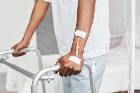 Close up of unrecognizable African-American man leaning onto walker in hospital, focus on iv drip catheter in hand, copy spaceの写真素材