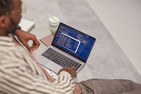 High angle view at young African-American man using laptop with IT code on screen while studying in college or working freelance, copy spaceの写真素材