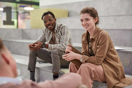 Group of students chatting cheerfully while relaxing in modern school lounge, focus on smiling young...