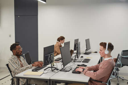 Wide angle view at group of young people using computers while working in office or school IT lab,...