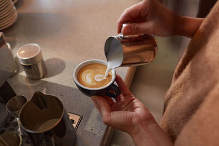Close up of unrecognizable barista creating latte art with cream while making fresh coffee in cafe...