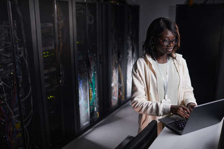 Portrait of African-American female network engineer using laptop while working in dark server room, copy spaceの写真素材