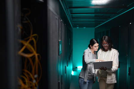 Wide angle portrait of two female IT engineers setting up server network while working in data center, copy spaceの写真素材