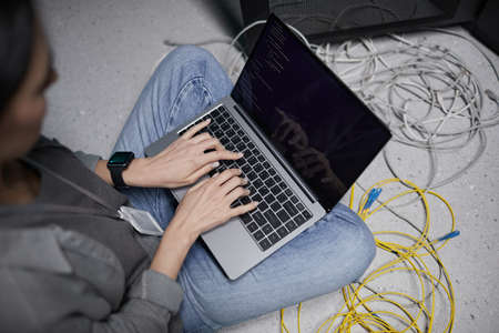 High angle closeup of female data engineer using laptop while sitting on floor in server room and setting up supercomputer network, copy spaceの写真素材