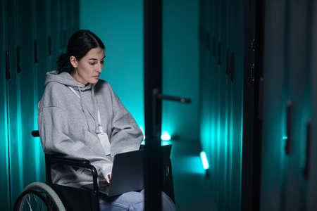 Portrait of disabled woman in wheelchair using laptop while working with supercomputer network in server room, accessible job concept, copy spaceの写真素材