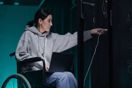Side view portrait of disabled woman in wheelchair working with supercomputer network in server room, accessible job concept, copy spaceの写真素材