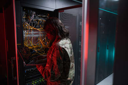 Back view at African-American woman managing computer network while working with supercomputer in server room lit by red light, copy spaceの写真素材