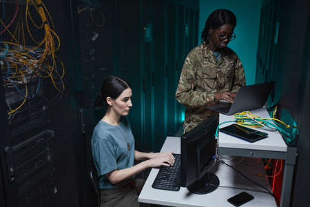 Portrait of two military young woman using computers while working together in server room and...