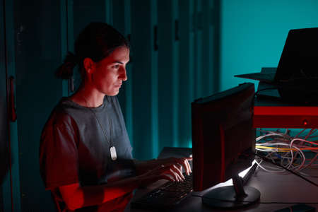 Side view portrait of female IT engineer using computer while working in server room lit by red...