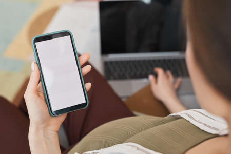 Close-up of young woman watching something on mobile phone while sitting on sofa at homeの写真素材