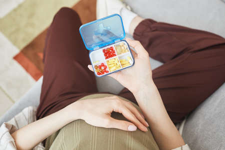 High angle view of pregnant woman holding box with vitamins and pills while sitting on sofaの写真素材