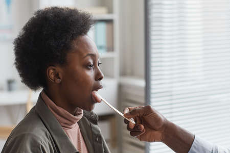 African woman opening her mouth while doctor examining her throat at hospitalの写真素材