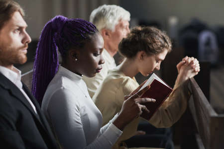 Group of people sitting on the bench in church and praying during ceremonyの写真素材