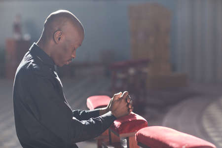African man sitting in front of the altar with eyes closed and praying in the churchの写真素材