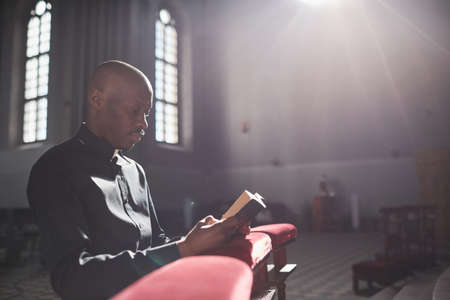African priest sitting in front of the altar and reading the Bible in the churchの写真素材