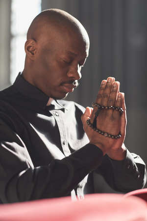 Serious African catholic with rosary beads praying in the churchの写真素材