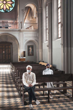 People in masks sitting on the bench in old beautiful church and prayingの写真素材