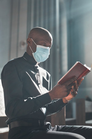 Young African priest in mask reading the Bible sitting in the churchの写真素材