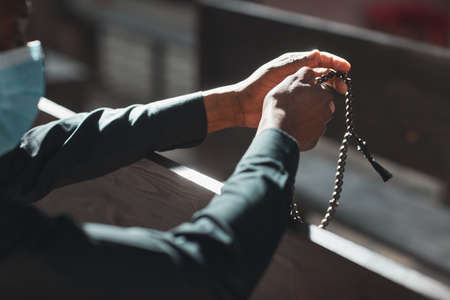 Close-up of priest in mask holding rosary beads while sitting in front of the altarの写真素材