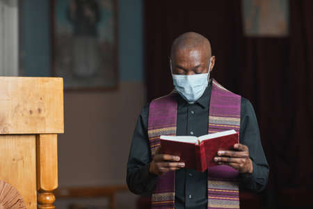 African priest in mask and in costume reading the Bible during mass in the church