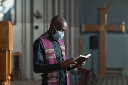 African priest in mask reading the Bible and holding the ceremony in the churchの写真素材