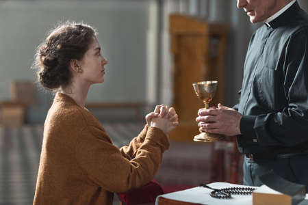 Faithful woman sitting in front of the priest and praying while he holding the cupの写真素材