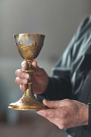 Close-up of priest holding the cup with wine while standing in the churchの写真素材