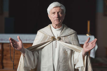 Portrait of senior priest in formal costume looking at camera and holding wedding in the church
