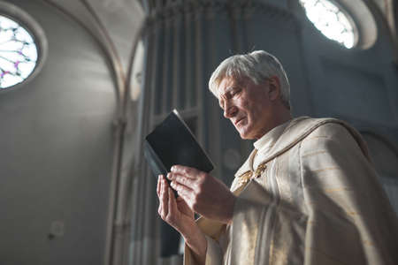 Senior priest in formal costume reading prayers while holding ceremony in the churchの写真素材