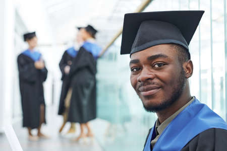 Close up portrait of young African-American man wearing graduation cap smiling at camera happily, copy spaceの写真素材