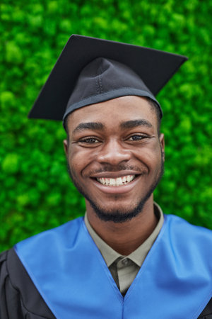 Vertical close up portrait of happy African-American man wearing graduation cap and smiling at...