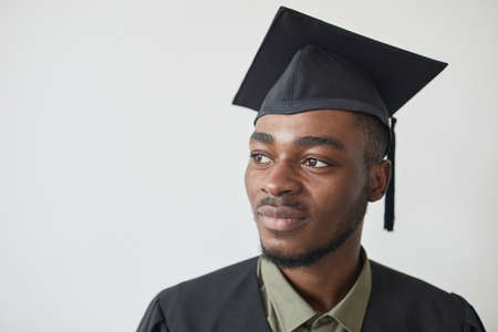 Head and shoulders portrait of confident African-Amerian man wearing graduation hat against white