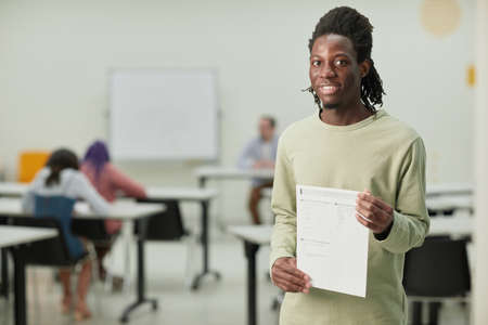 Waist up portrait of teenage African-American boy in school classroom smiling happily at camera and holding test certificate, copy spaceの写真素材