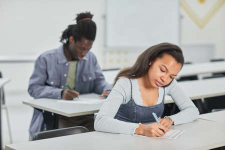 Students taking test in school class with focus on young African-American woman sitting at desk in front, copy spaceの写真素材