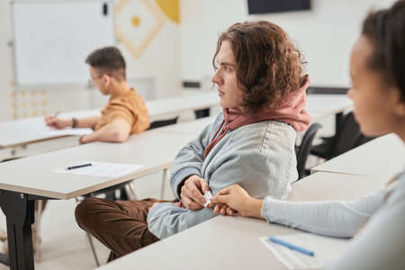 Side view portrait of two teenagers passing note in class during school lesson, copy space