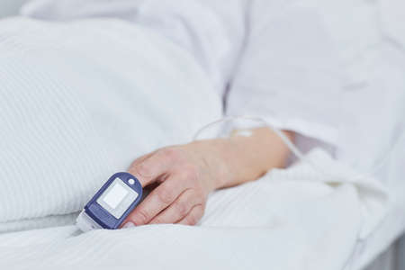 Close-up of patient lying on bed with medical pressure equipment on her finger