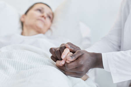 Close-up of African doctor holding hand of his patient and supporting her at hospitalの写真素材