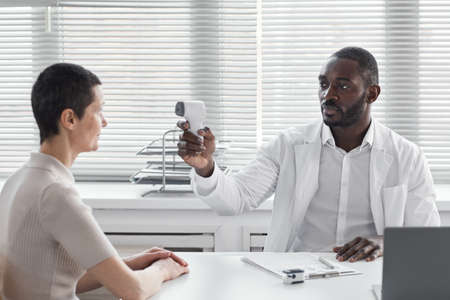 African doctor checking the temperature of his patient during her visit at hospital
