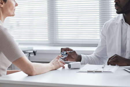 African doctor checking the pulse of woman while they sitting at the table at hospitalの写真素材