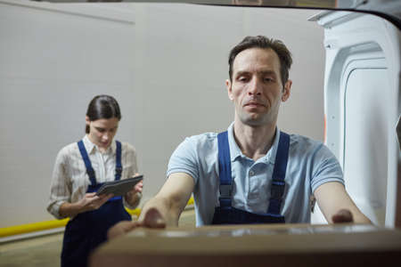 Young man shipping the box in the lorry with woman registrating it in the backgroundの写真素材
