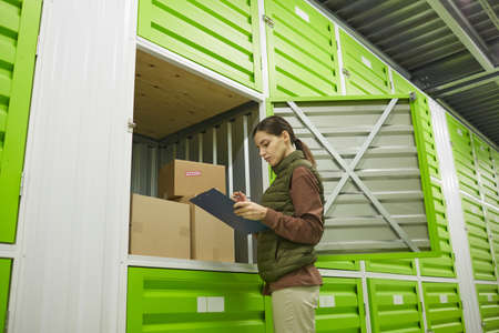 Young woman making notes in document and checking the parcels in storage