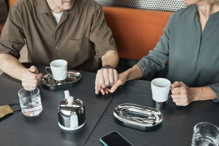 Close-up of mature Caucasian couple sitting at table and holding hands while drinking tea together in coffee shopの写真素材
