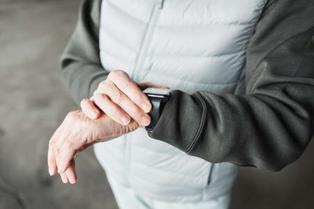Close-up of unrecognizable woman in warm wear checking pulse on smart watch after outdoor trainingの写真素材