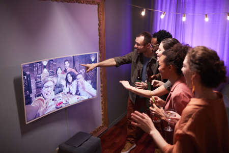 Diverse group of young people speaking to friends online while enjoying party at home